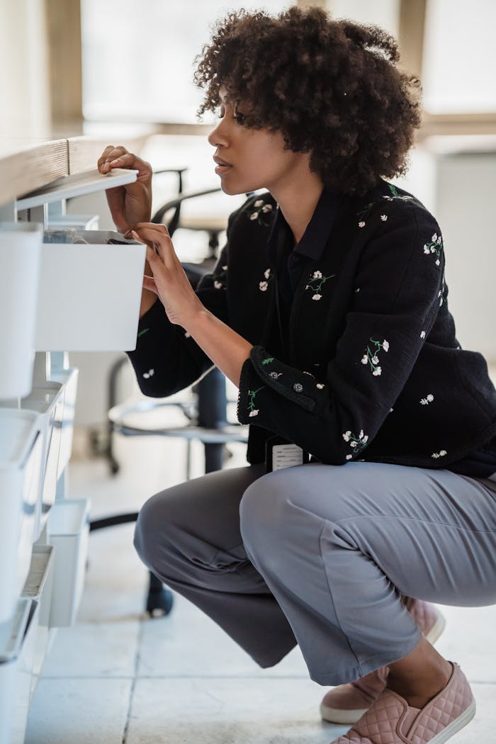 Woman organizing office supplies in drawer, showcasing tidy workspace habits.